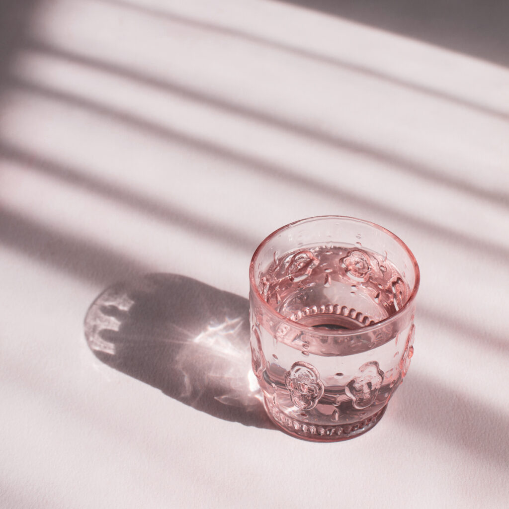 Pink glass on pink background, glass is filled with water. Optimal hydration and knowing what and when to drink are key to well-being and performance.