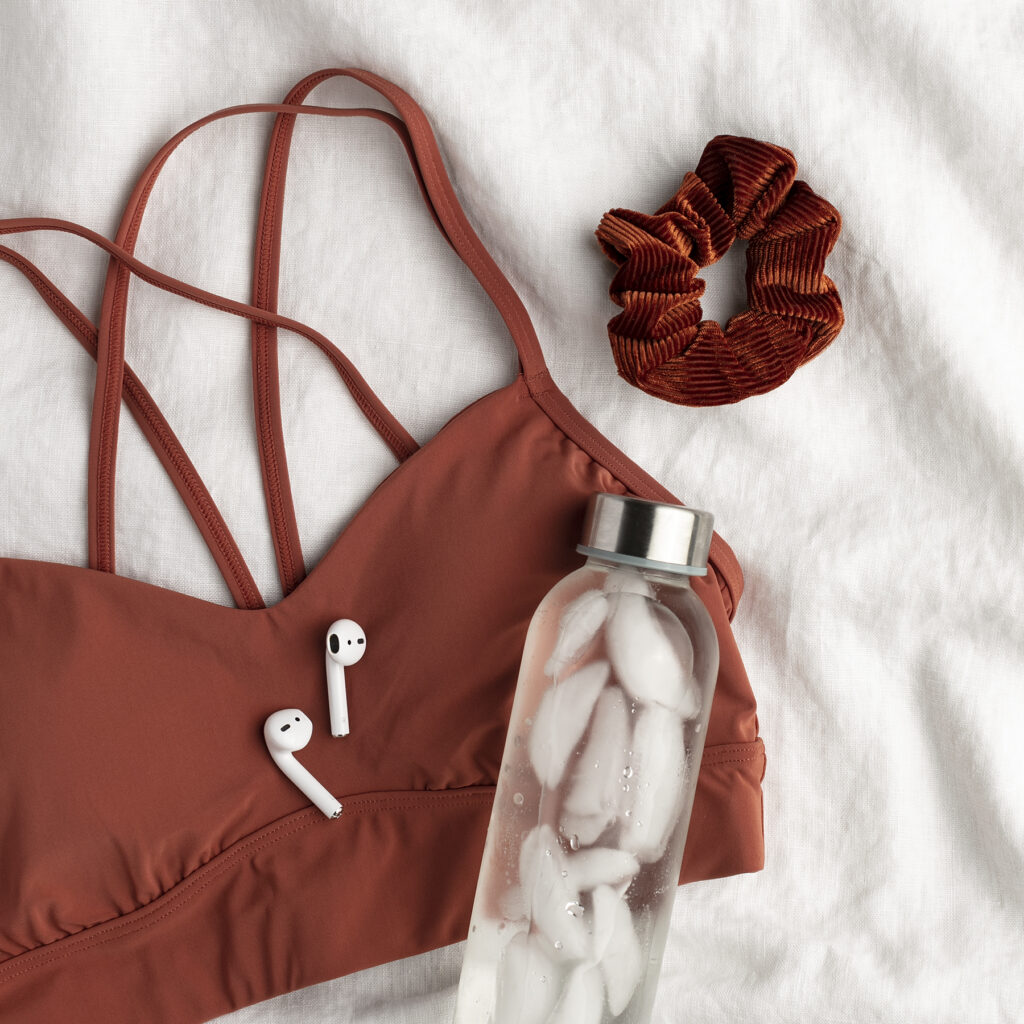 Burgundy scrunchy and sports bra, ear pods and a glass reusable water bottle filled with iced-water. Optimal hydration during exercise can boost performance.