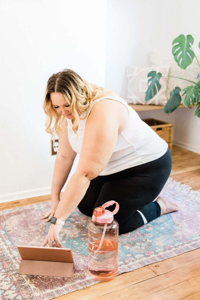 Larger fair skinned woman choosing a yoga workout on her ipad in her home as she does her yoga home practice for the day