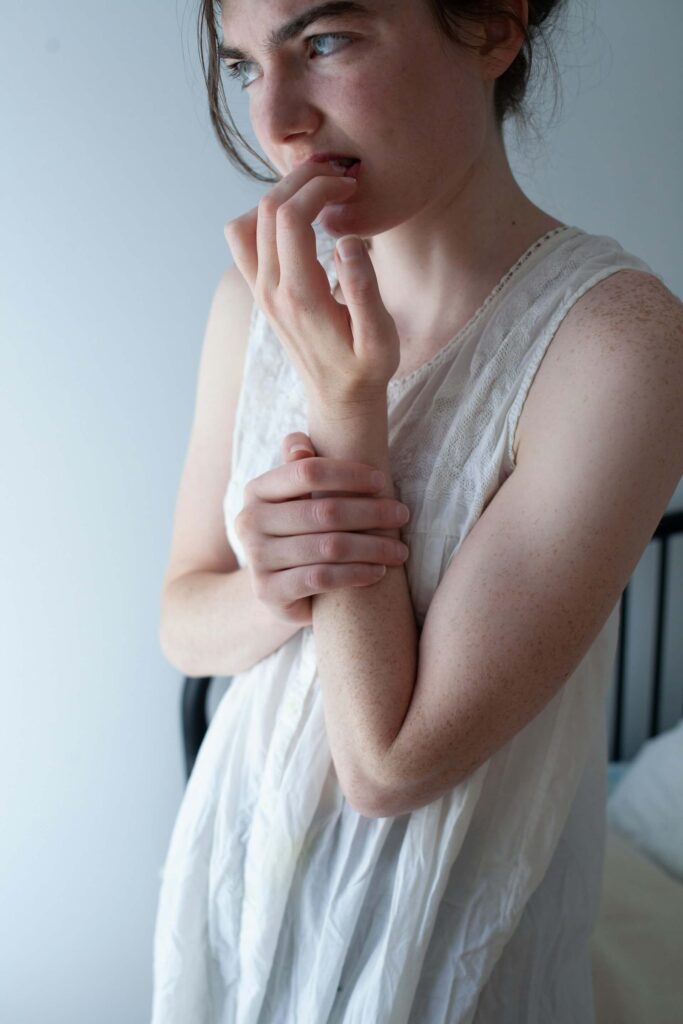 young woman in white nightgown biting her nails from stress and worry