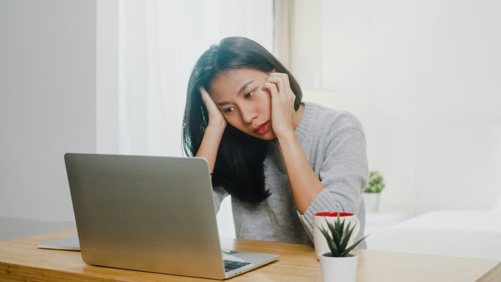 young asian woman leaning on her desk looking at her computer in a tired manner. Too many emails, deadlines and to-dos cause stress in everyday life.