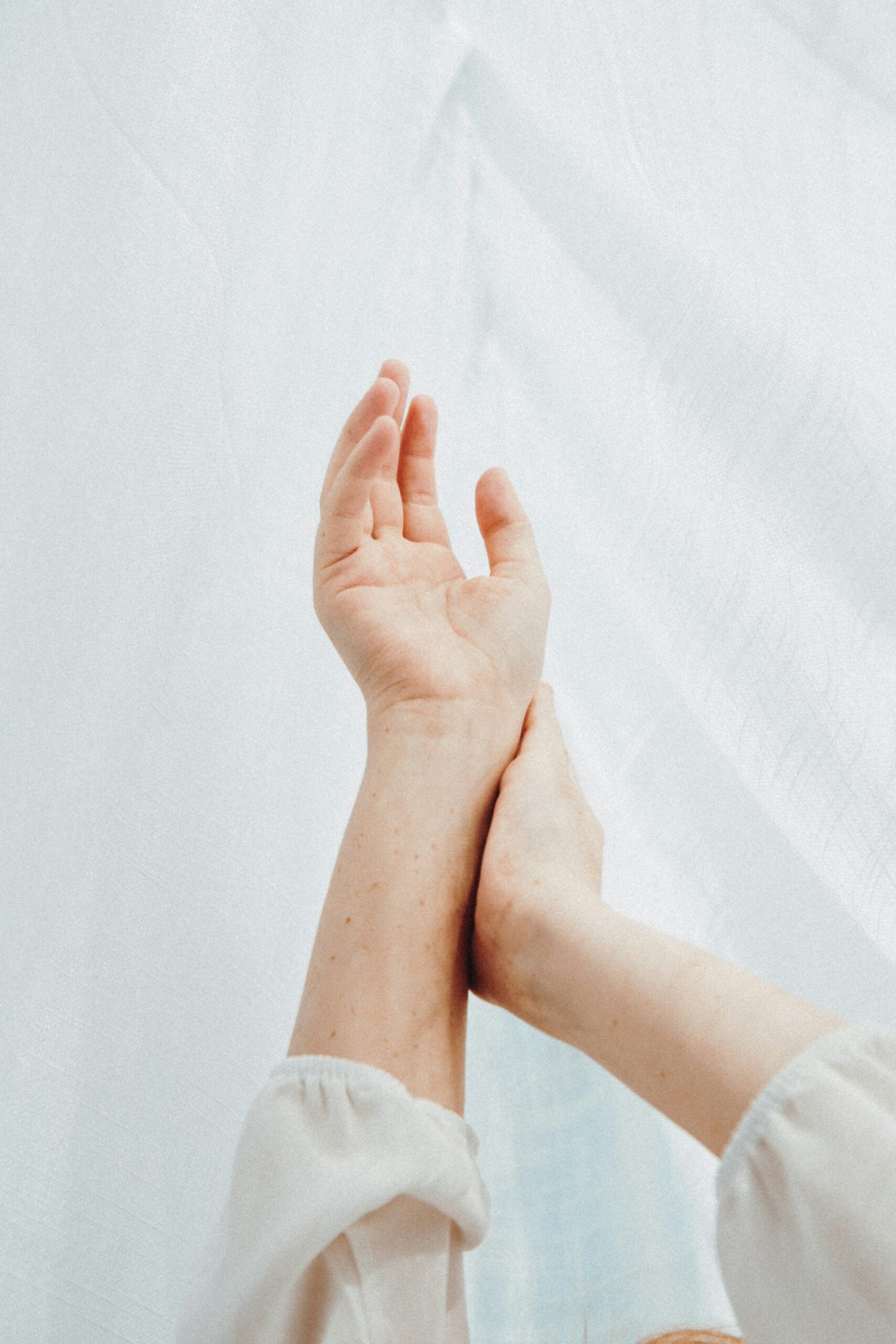 wrist pain in yoga, pair of arms and hand reaching up on a white background