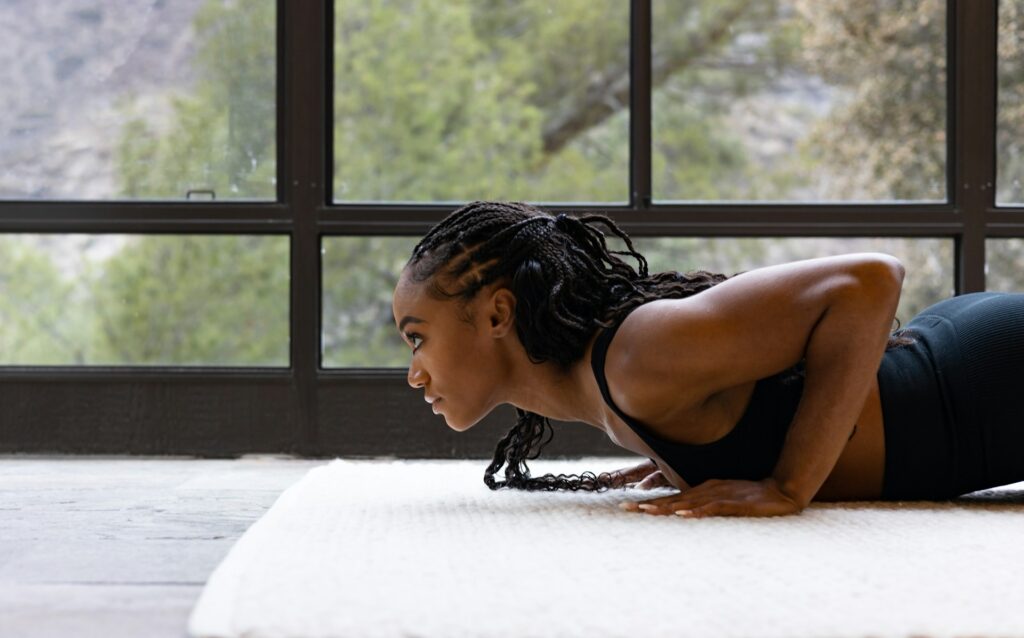 black woman doing chaturanga on a white carpet demonstrating poses that can cause wrist pain in yoga